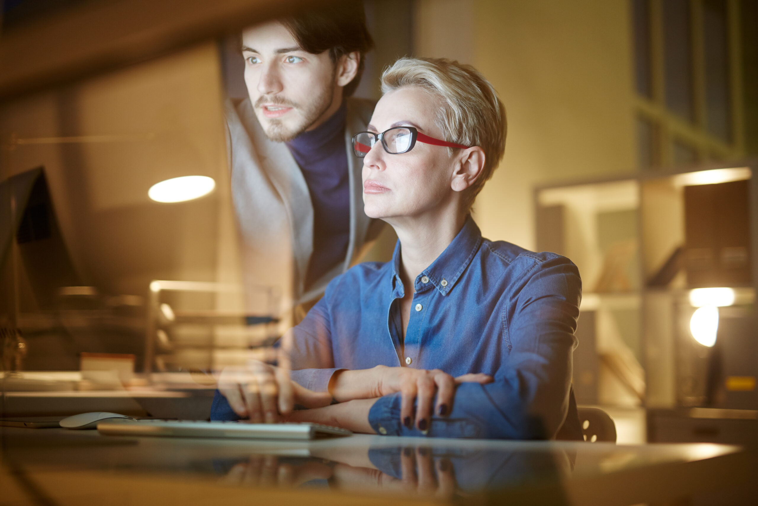 Mature and young colleagues watching attentively online conference in the evening